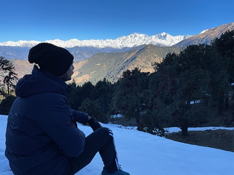 A South Asian man sitting atop a snow-covered hill in Chandrashila trek, Uttarakhand