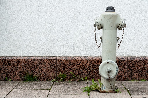A white fire hydrant is situated on the side of a concrete sidewalk in an urban area