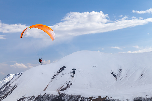 Gudauri, Georgia - May 1, 2019: Paragliders fly in front of snowy peaks of Caucasus on a sunny day
