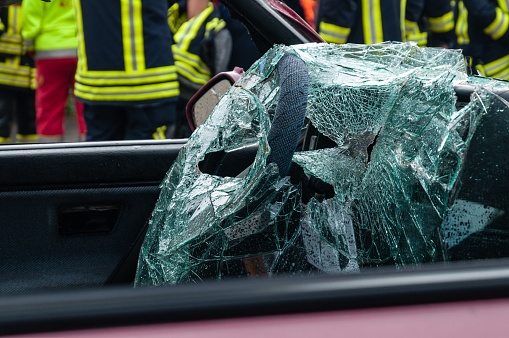 A firefighter stands behind a car with a damaged, shattered windshield, assessing the situation