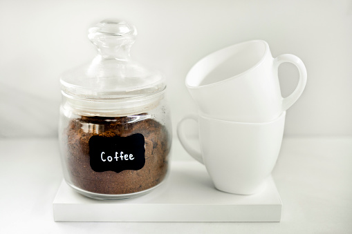 Freshly ground coffee in a glass container with two white caps on the white background. Breakfast coffee concept. Process of making coffee at home.