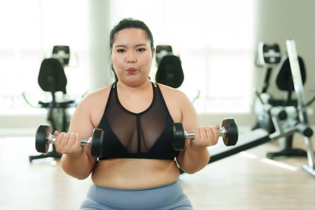 istock Chubby Asian girl Perform a seated exercise by lifting dumbbells with both arms. trying to lose weight and reduce excess fat Serious face Committed to exercising Overweight woman exercising in gym. 1798143904