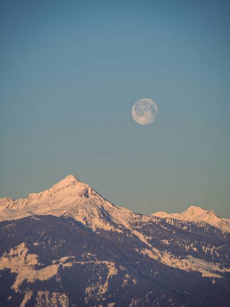 full moon setting over a snow covered winter mountain peak in the alps - light effect full moon mountain peak european alps imagens e fotografias de stock