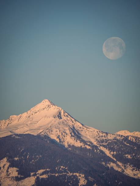 istock Full moon setting over a snow covered winter mountain peak in the Alps 1798144460