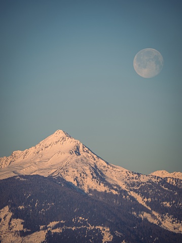 Full moon setting over a snow covered winter mountain peak in the Alps, Carinthia, Austria