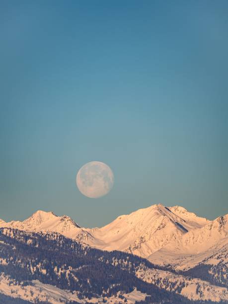 full moon setting over a snow covered winter mountain peak in the alps - light effect full moon mountain peak european alps imagens e fotografias de stock