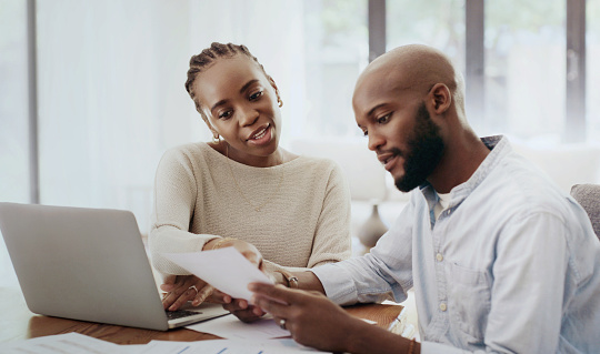 Couple, laptop and reading documents in home for budget, finance portfolio or mortgage loan. African man, woman and bills for online banking, rent or savings of investment, taxes and insurance policy