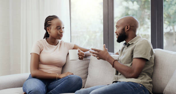 istock Couple, communication and smile on sofa with coffee for relax, discussion and peace on weekend in living room. Black people, man and woman with conversation or talking on couch for bond, love or care 1798152527
