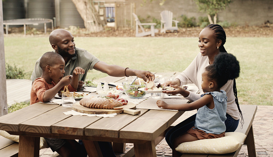 Food, picnic and a black family in the garden of their home together for health, diet or nutrition. Love, smile or happy with a mother, father and children eating a meal outdoor in the backyard