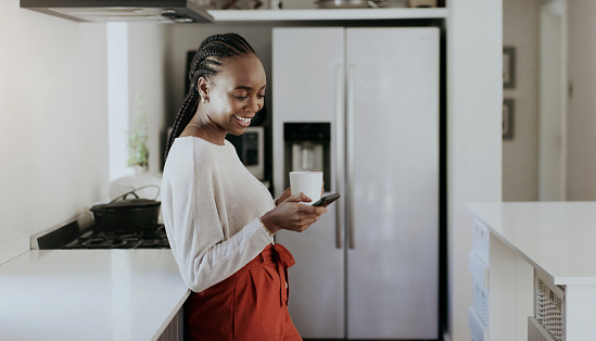 Woman, coffee or typing on smartphone in kitchen for social network, update multimedia subscription or search web. Happy african girl drinking tea, download mobile app or reading notification at home