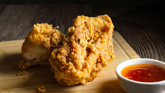 Crispy fried chicken on a wooden plate with chili sauce on a wooden board background