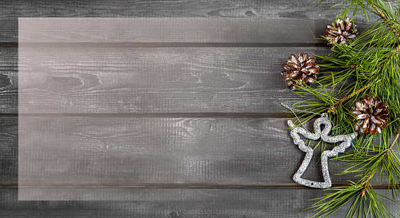 Wooden Christmas background with natural pine needles, cones and silver angel. Frame, banner, postcard.