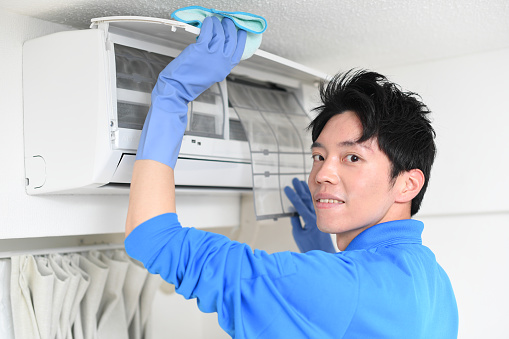 Young Asian man from a house cleaning company cleaning the air conditioner in the house
