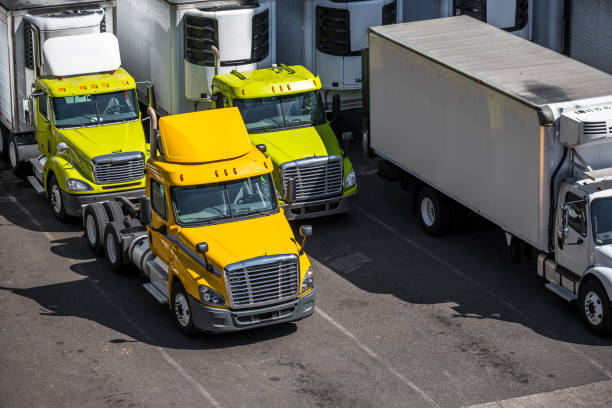 istock Day cab powerful big rig semi trucks with refrigerator semi trailers standing on the warehouse parking lot waiting for the next load for local deliveries 1798211133