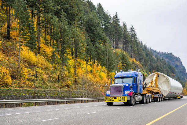 istock Blue big rig bonnet semi truck tractor with oversize load sign transporting part of oversized wind turbine pillar running on the picturesque autumn road in Columbia Gorge 1798211694