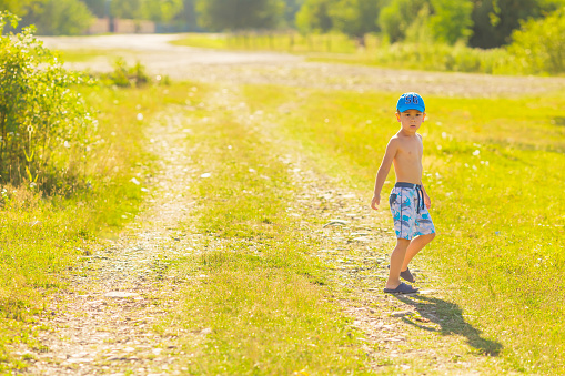 Boy in summer day standing on a dirt road passing the village