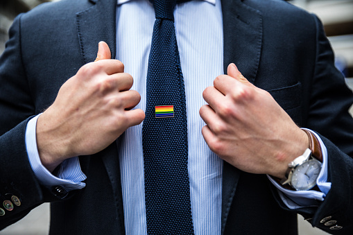 Business man adjusting his suit and wearing a necktie with a rainbow flag.