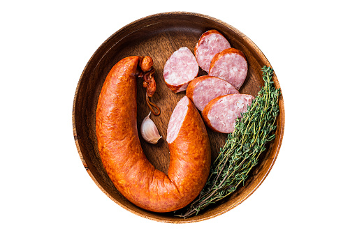 Sliced cold Smoked sausage in a wooden plate with thyme.  Isolated, white background. Top view