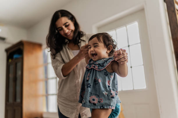 Mother supporting her daughter to take the first steps in the playroom