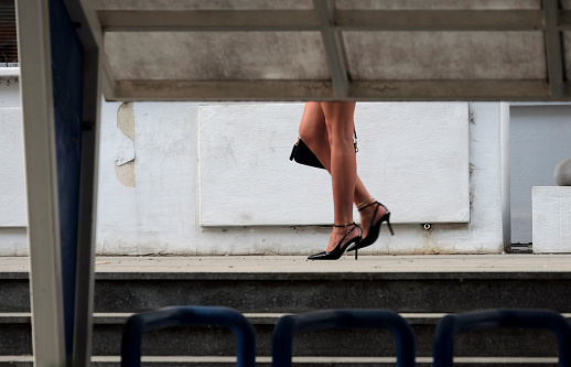 Legs of a woman in high heels walking by holding a handbag