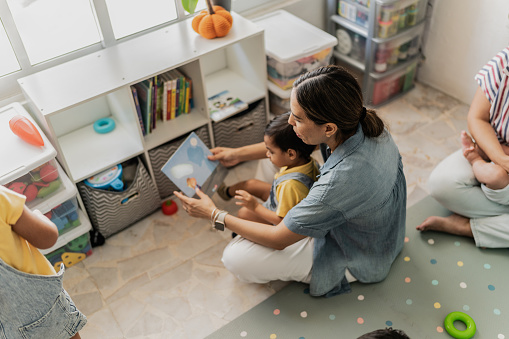 Mid adult woman reading a book to her son in the playroom