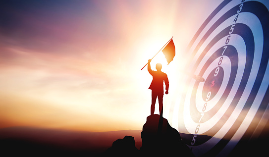 Silhouette of businessman holding a flag on top mountain with a target board showing victory. concept of success according to work goals and outstanding business leadership