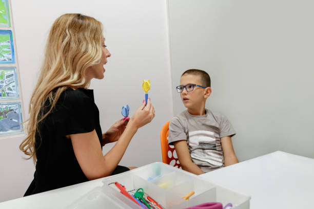 istock Elementary age boy in speech therapy looking at female doctor holding special tools for practicing 1798252059