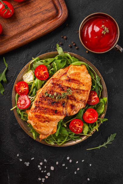 peito de frango grelhado com rúcula e tomates em um prato, vista superior, fundo de comida preto - fillet meat portion fillet steak - fotografias e filmes do acervo