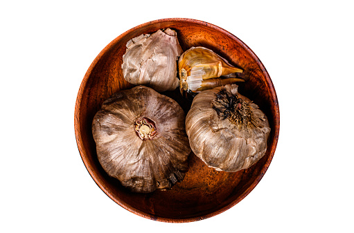 Bulbs and cloves of fermented  black garlic in a plate.   Isolated, white background