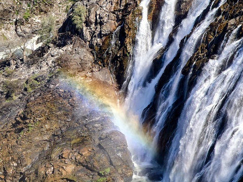 A stunning landscape featuring a majestic waterfall cascading down a rocky mountain, with a vibrant rainbow arching in the distant sky above