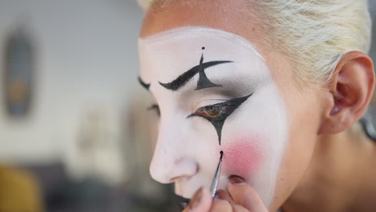 Young woman, a mime artist, applying face paint while getting ready for pantomime show.