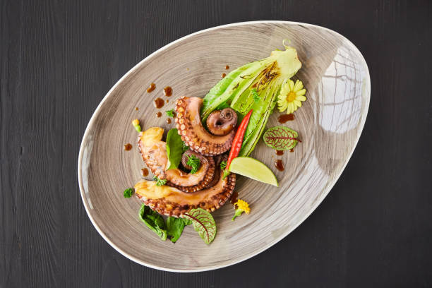 istock Seafood octopus or squid tentacles on a plate decorated with lime and lettuce. Decoration of flowers and herbs spices. A dish from the chef for serving 1798301509