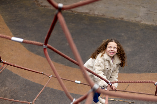 High-angle view shot of a young girl climbing a rope structure looking at the camera. She is wearing warm clothing on a cold winter morning. The park is located in Gateshead.

Videos are also available for this scenario.
