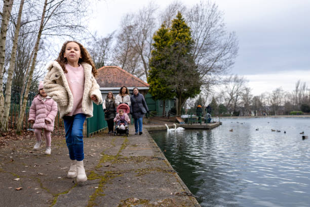 Full shot of a young girl running ahead of her family lakeside in a public park. They are all wearing warm clothing on a cold winter morning. The park is located in Gateshead.\n\nVideos are also available for this scenario.