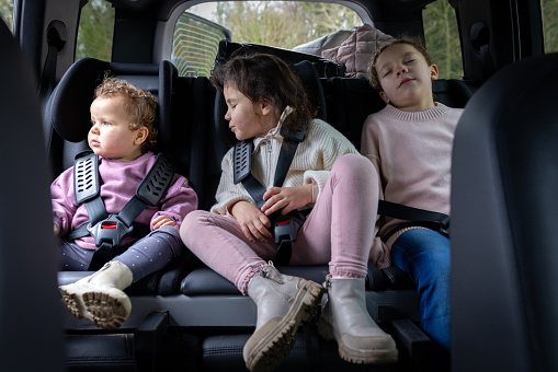 A three-quarter-length shot of three sisters sitting in the back of a car asleep seatbelted in. They are looking at the camera all wearing casual clothing ready for a day out.

Videos are also available for this scenario.