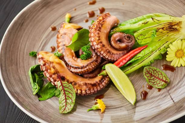 istock Seafood octopus or squid tentacles on a plate decorated with lime and lettuce. Decoration of flowers and herbs spices. A dish from the chef for serving 1798338550