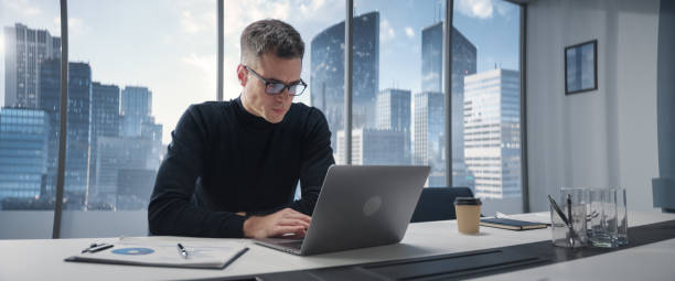 istock Caucasian Businessman Standing In Corner Office And Thinking Infront Big Window With Megapolis Cityview. Professional CEO Sitting Down At Desk And Starts Working On Laptop Computer. 1798342954