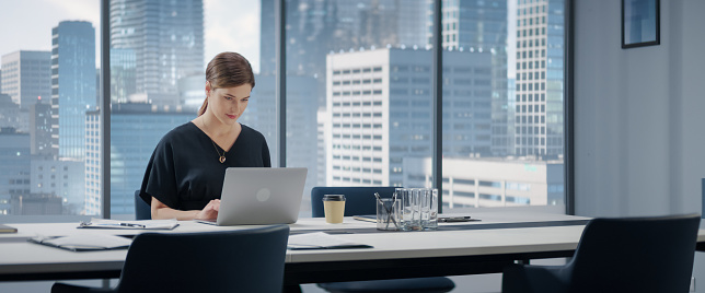 Portrait of Successful Caucasian Businesswoman Working on Laptop Computer in Her Big City Corner Office. Professional Female Digital Entrepreneur does Data Analysis for e-Commerce.