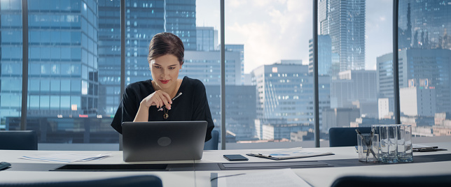 Portrait of Young Successful Caucasian Businesswoman Sitting at Desk Working on Laptop Computer in City Office. Female Manager Plan Investment Strategy for e-Commerce Project.
