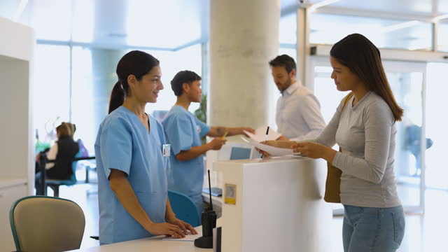 Healthcare workers at the reception desk of a hospital receiving patients and handing them forms before their appointments