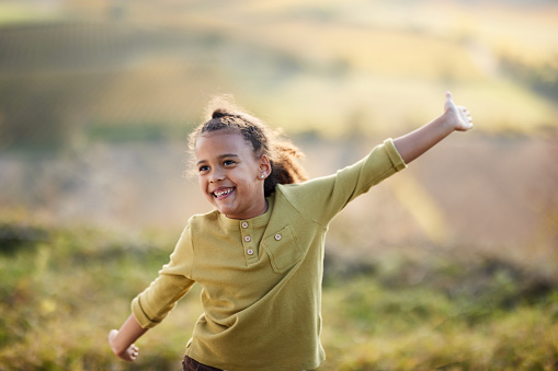 Happy African American girl having fun with her arms outstretched in nature. Copy space.