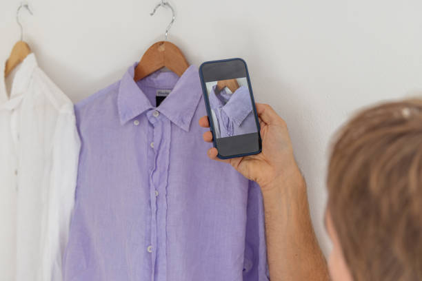 Side hustles, Man selling his used clothes online, using mobile phone to take pictures stock photo
