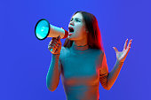 Portrait of angry girl, teenager, student announce in megaphone about sales season start against blue background in neon light.