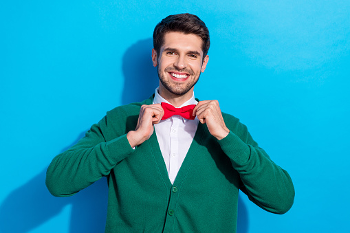 Photo of pretty charming guy dressed xmas green cardigan adjusting red bow tie isolated blue color background.