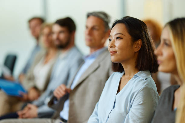 Smiling Chinese businesswoman attending a seminar with her colleagues. Young smiling Chinese businesswoman and her colleagues attending an education event in the office. corporate business stock pictures, royalty-free photos & images