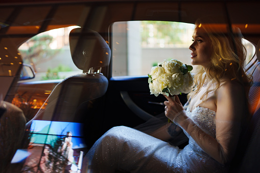 a beautiful and happy bride with a bouquet in a car through the glass.