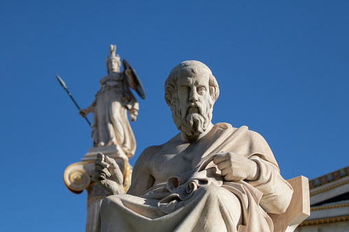 Marble statue of Greek philosopher Plato. Statue of goddess Athena on background.