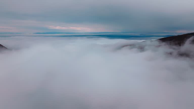 Aerial view of vibrant sunrise over white dense fog with distant dark  mountains on horizon