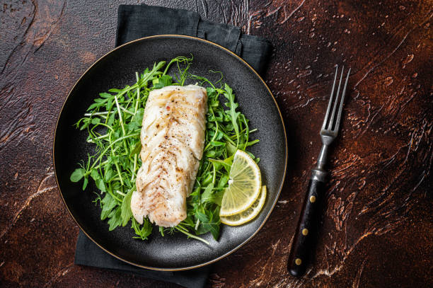 istock Grilled cod fish fillet served with green salad in a plate. Dark background. Top view 1798442484