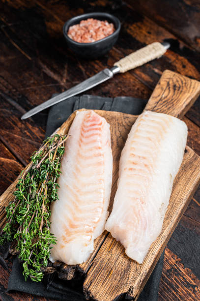 istock Cod fish fillets, raw codfish with thyme on wooden board. Wooden background. Top view 1798442485